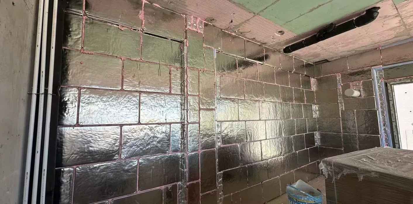 Stainless steel VIP panels installed on the room side of a wall, with the layout coordinated around windows and services. Photograph from the documented building application.